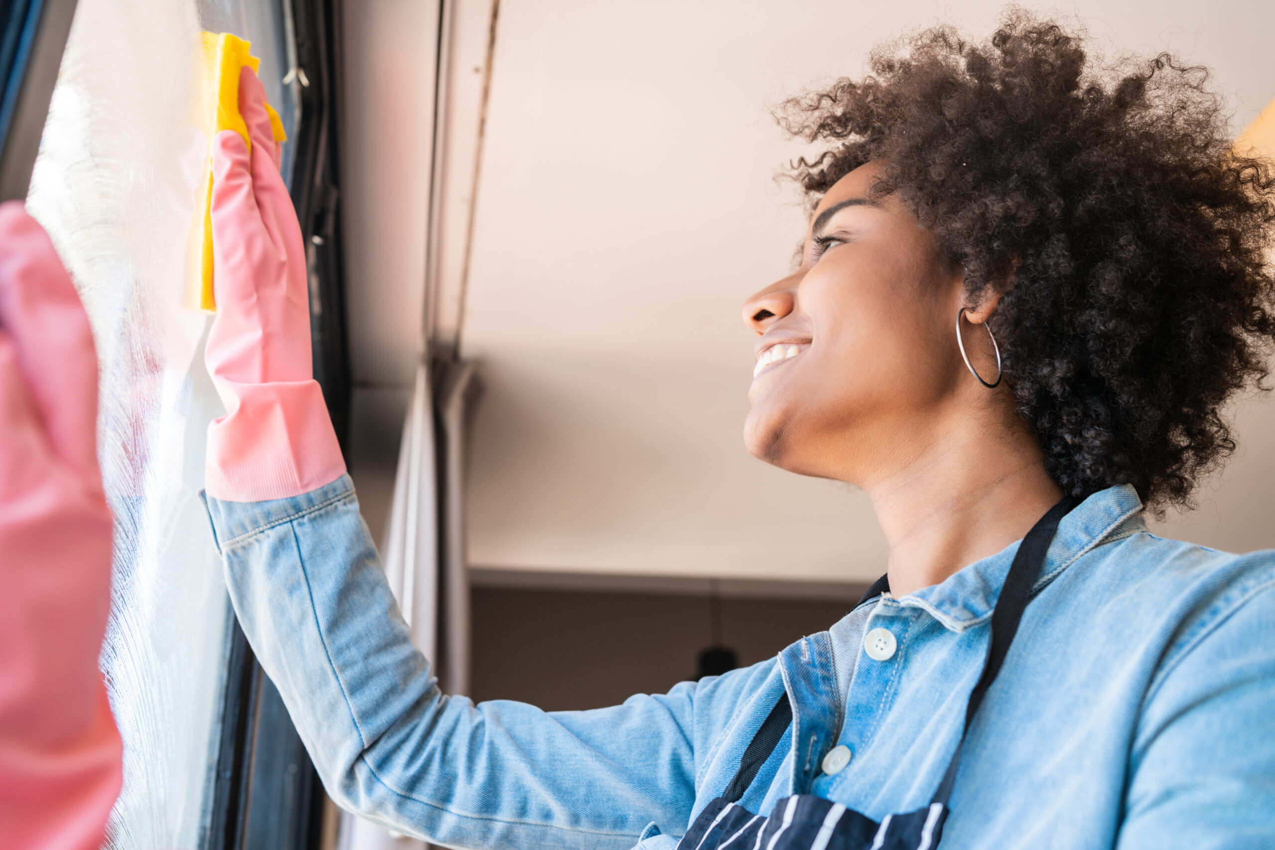 Afro woman cleaning window with rag at home.